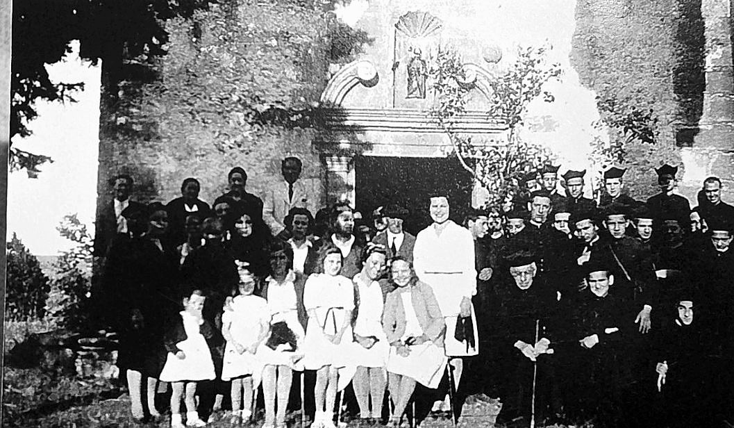 Fotografia antiga en blanc i negre de nenes de comunió i clergat al portal de l'ermita de Sant Jaume de la Coma